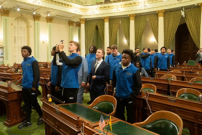 Team members and coaches of the College of San Mateo football team on the floor of the State Assembly. 