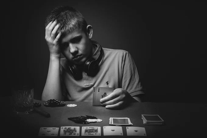 Black and white photo of a young boy playing poker and looking very forlorn. 