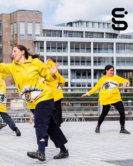 People wearing yellow anoraks are in various dancing poses.