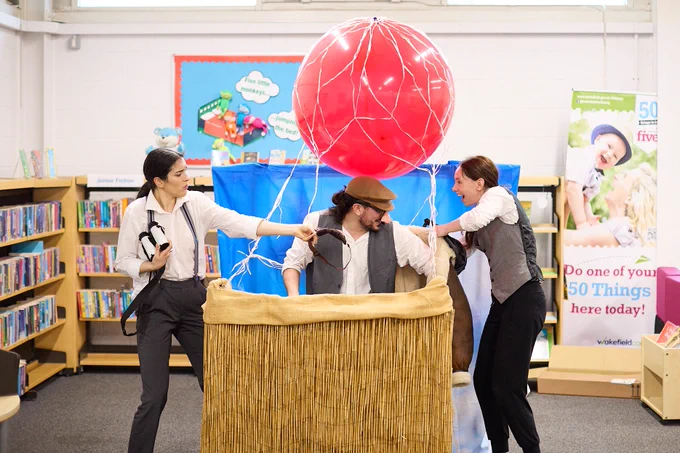 Tmesis Theatre performing Up and Away in a library setting. Featuring three actors performing with a hot-air balloon.