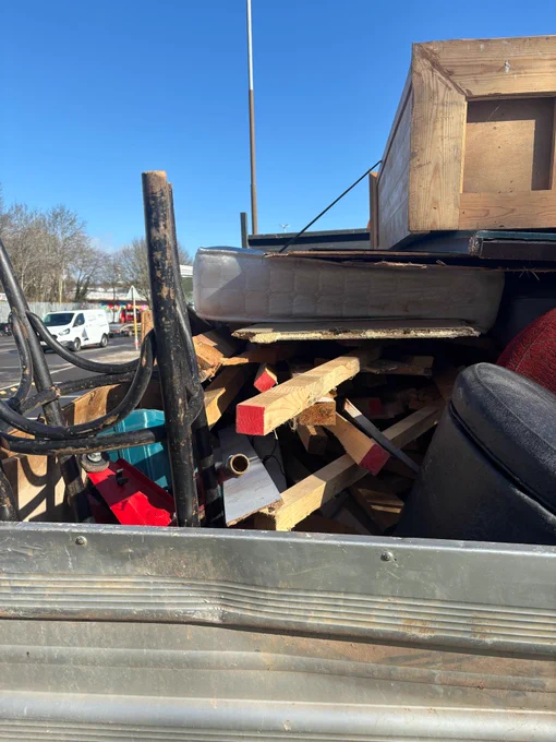 Side view of a flatbed truck overloaded with household goods, not netted or strapped down safely.