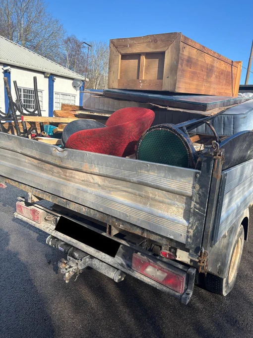 Rear view of a flatbed truck overloaded with household goods, not netted or strapped down safely.
