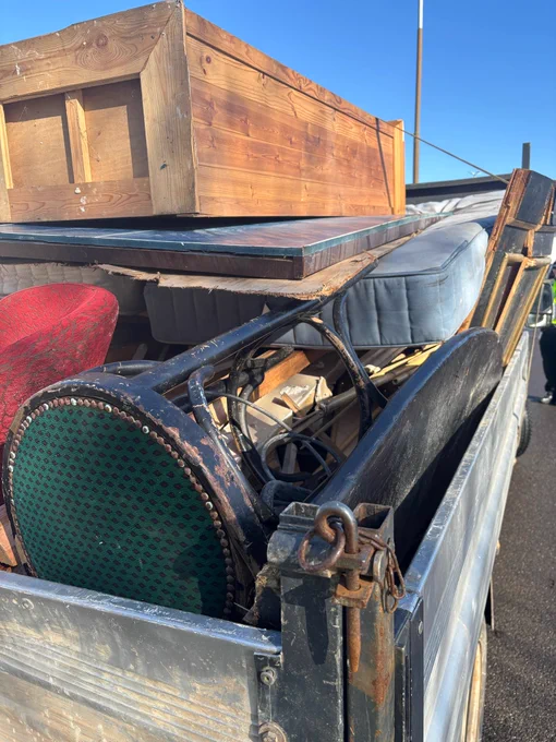 Rear view of a flatbed truck overloaded with household goods, not netted or strapped down safely.
