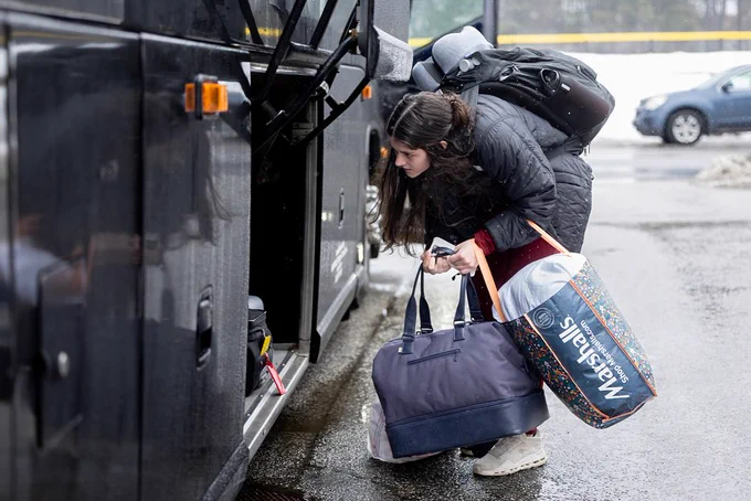 A student (on right) bends down to put her bags underneath the bus.