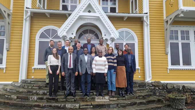 Delegates at the HEPI project meeting in Norway, standing on steps outside a yellow building. 