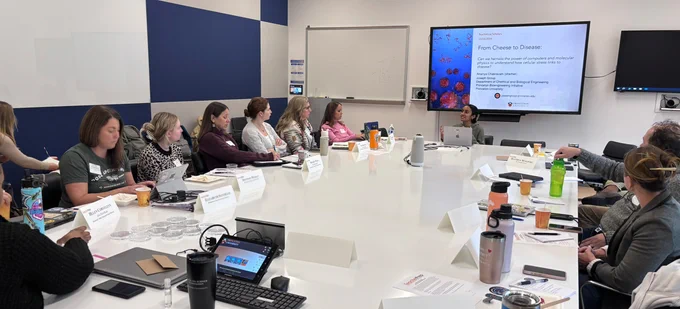 teachers seat around a table and listen to a grad students 