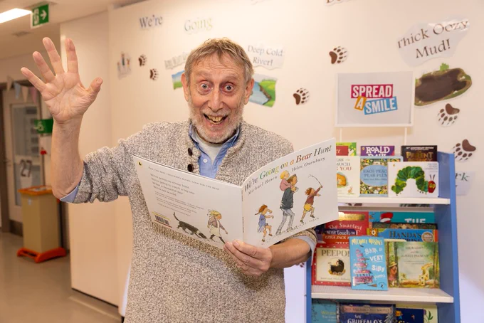 Michael Rosen holding his book 'We're Going On A Bear Hunt' next to one of the donated libraries