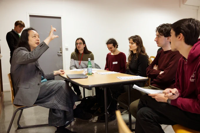 Audrey Tang gestures while talking to students at a table.