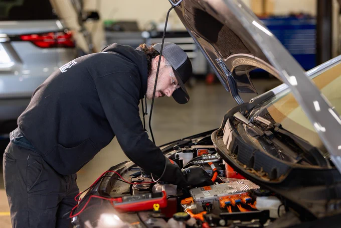 A Tesla service technician works on a car's engine in a garage.