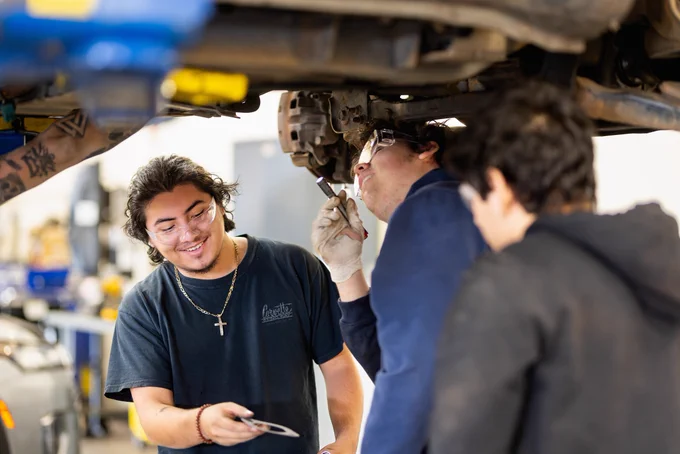 Three mechanics working together under a car in a repair shop.