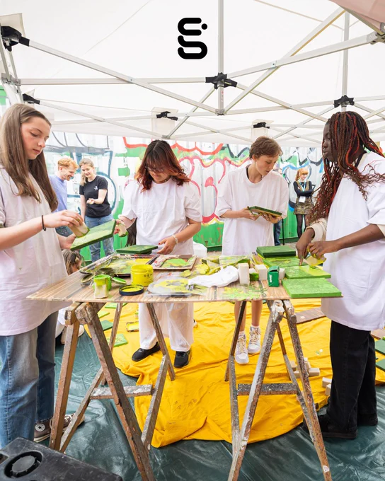 Four people stand around a table, doing a printing activity.