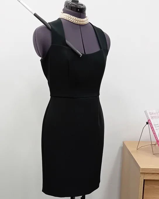 A dress form is wearing a little black dress, a pearl choker, and tucked into the dress strap is a paper cigarette in a long black holder.