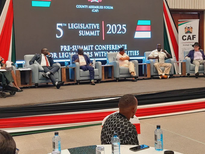 Dr. Oliver Waindi speaking at the conference.  He is seated alongside 5 other panellists 