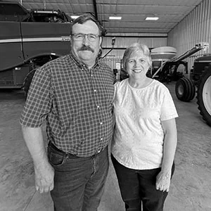 Two smiling adults standing in a warehouse with agricultural machinery in the background.