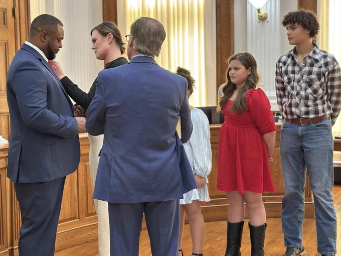 Woman helps pin man who has just been sworn in while his family looks on