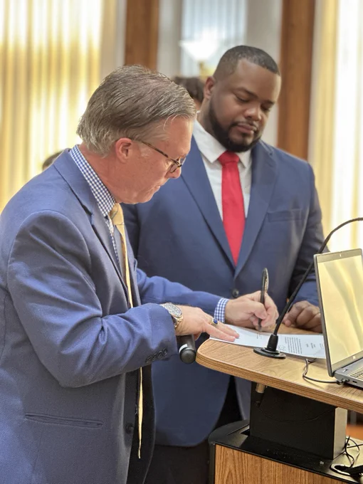 One man signs a paper while the other man waits to sign
