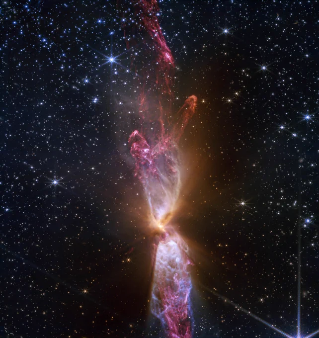 At the centre is a thin vertical cloud known as Lynds 483 (L483) that is roughly shaped like an hourglass with irregular edges. The lower lobe is slightly cut off. The top lobe is seen in full, petering out at the top.
