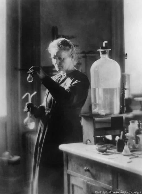 Marie Curie in a laboratory, examining a scientific glass apparatus.
