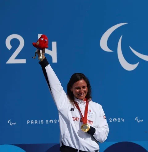 Dame Sarah Storey from Great Britain holding up a gold medal and a red mascot at the Paris 2024 Paralympic Games podium.