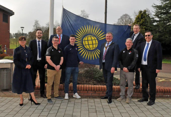 Small group of people standing beside a flag outside