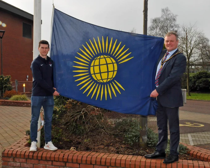 Two males standing beside a flag outside