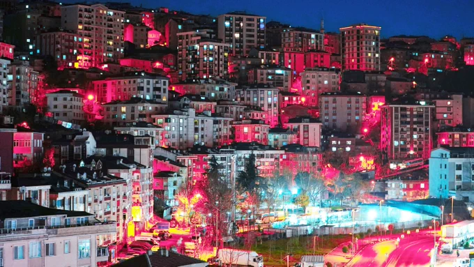 A night image of an urban area showing tightly clustered buildings on a hill. (Photo Credit: selcuk s on Unsplash; modified by the Army Geospatial Center.)