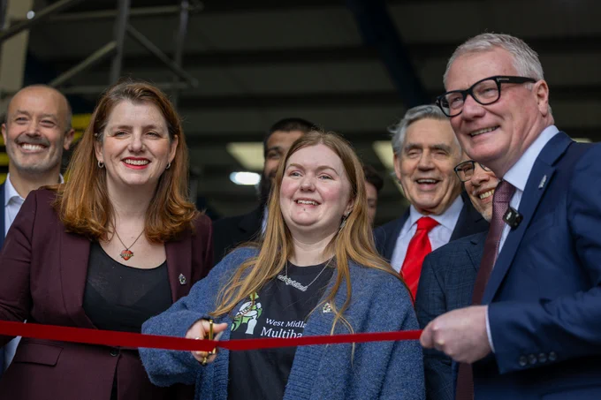 Photograph of a group of people (men and women) stood together cutting a red ribbon. 
