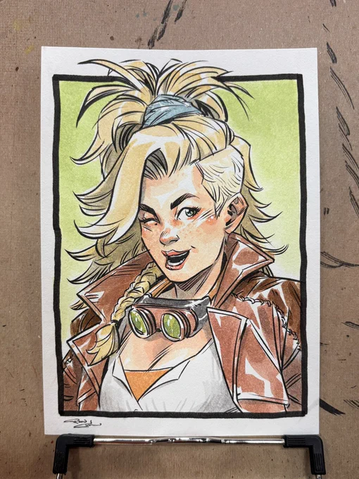 Watercolor portrait of Gemma from Monster Hunter Wilds. She's a beautiful blonde woman with tall hair, leather jacket, and googles hanging around her neck. She's winking at the viewer with a smile.
