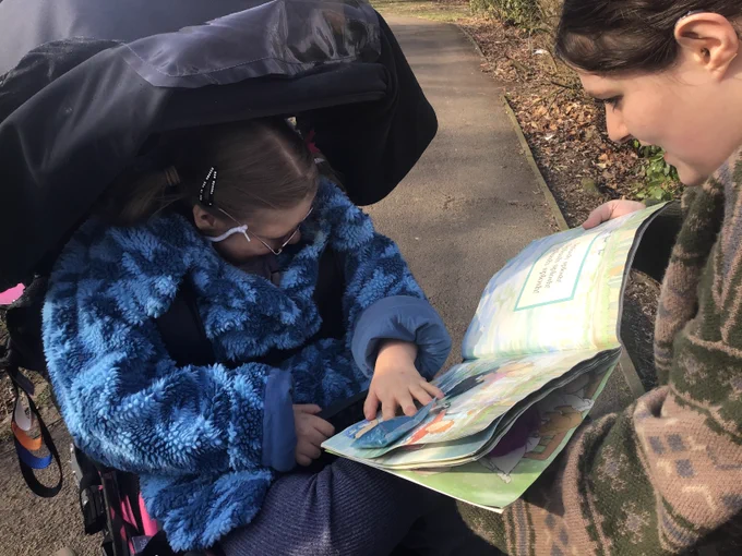 A young woman wearing a blue taking part in a sensory story activity by reaching out and exploring the pages.  