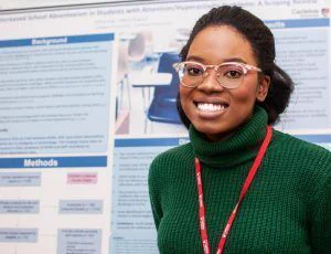 A student smiling in front of their poster presentation at the I-CUREUS and SaPP Showcase