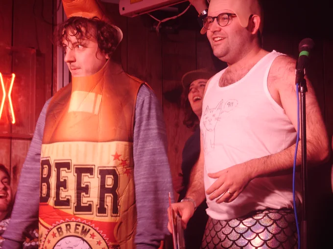 Tom dressed as a beer bottle, beside Adam in a bald cap and hand drawn cat vest