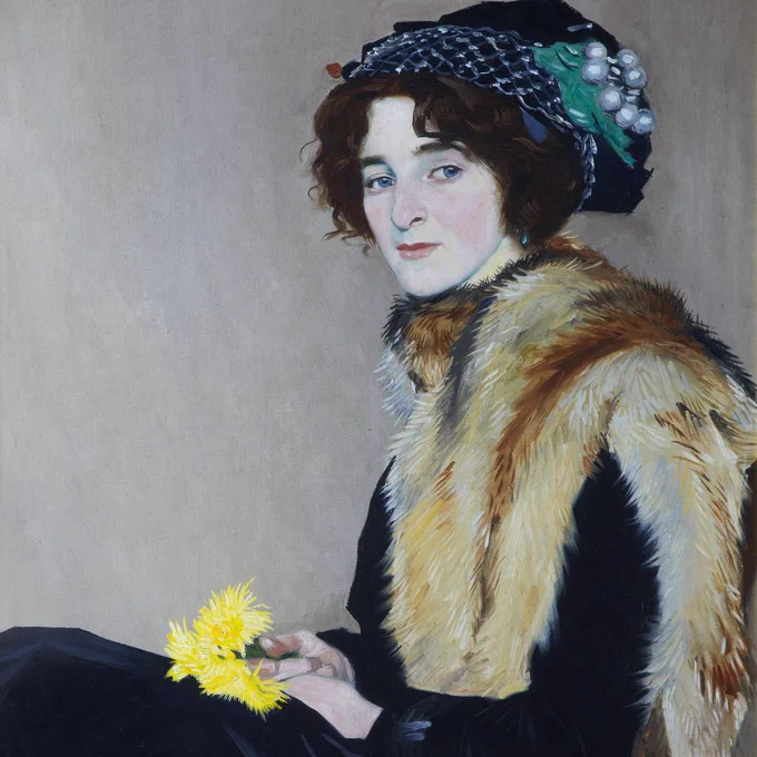 This painting is Girl with a Fur Cape by William Strang (1859 - 1921). It shows a woman seated in profile facing to the left, with her face turned towards the viewer. She has pale skin, blue eyes and dark red hair, which is pinned under a dark blue hat. She wears a black velvet dress, and has an orange-brown fox fur cape pinned wrapped around her shoulders. She rests her hands in her lap, and is holding a small bunch of yellow flowers.
