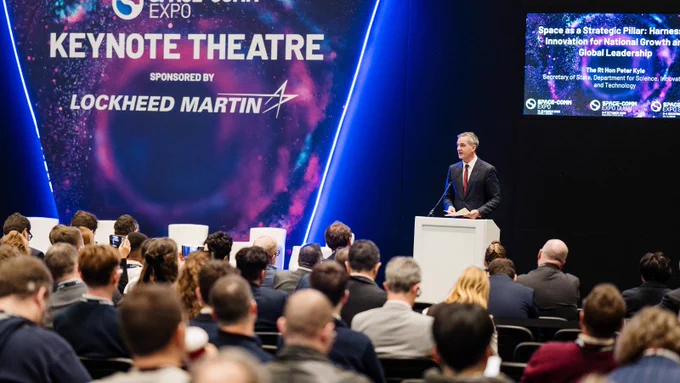 Secretary of State, Peter Kyle (right) speaks on stage in front of a large audience at the Space Comms Expo. 
