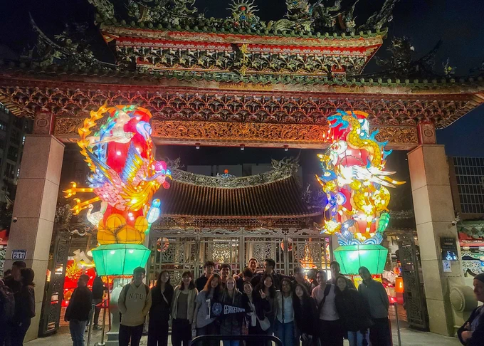 Night view of Longshan Temple in Taiwan with colorful, illuminated dragon sculptures at the entrance, surrounded by visitors.