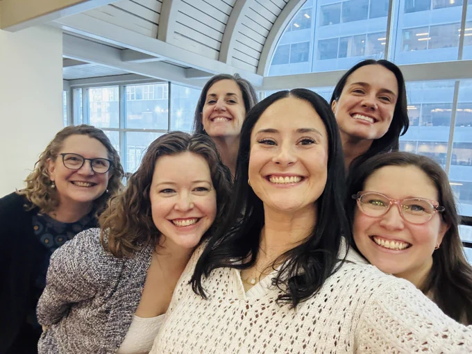 Six people are clustered together, smiling at the camera, while the person in the front center takes a selfie of them