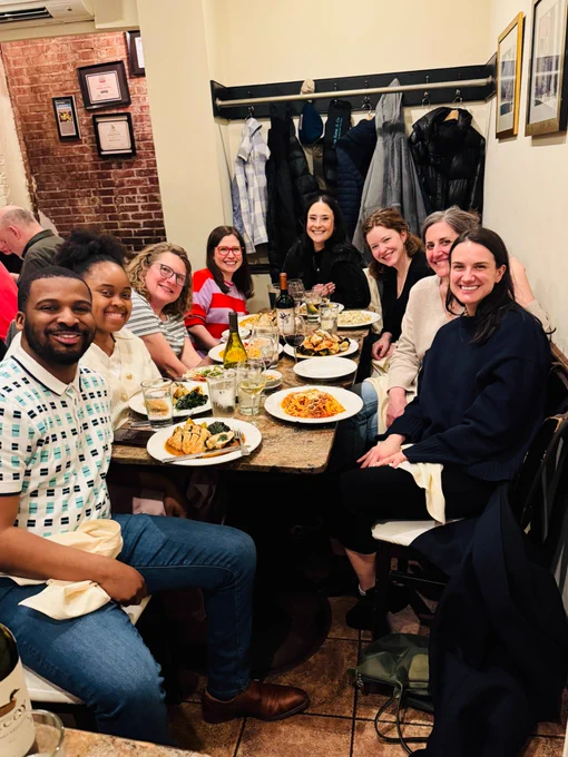 Eight people smile around a long dinner table. 