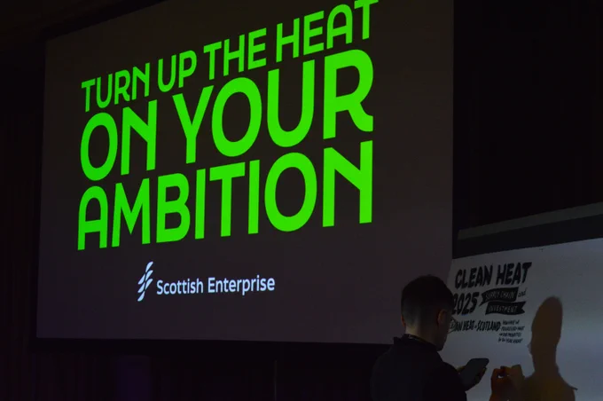 The words 'Turn up the heat on your ambition' in green on a large TV screen
