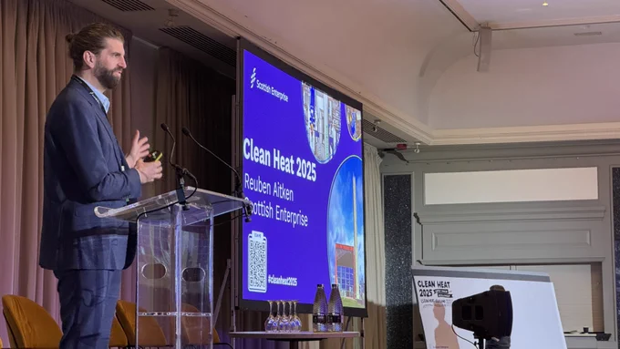 Image of a man speaking on stage, standing behind a podium, beside a screen that says 'Clean Heat 2025'