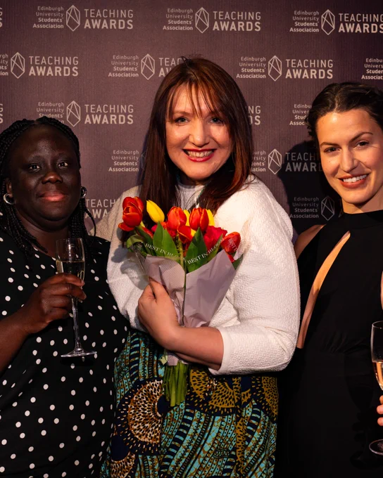 3 staff members at the teaching awards, they are all smiling at the camera and the one in the middle is carrying a bouquet of flowers.