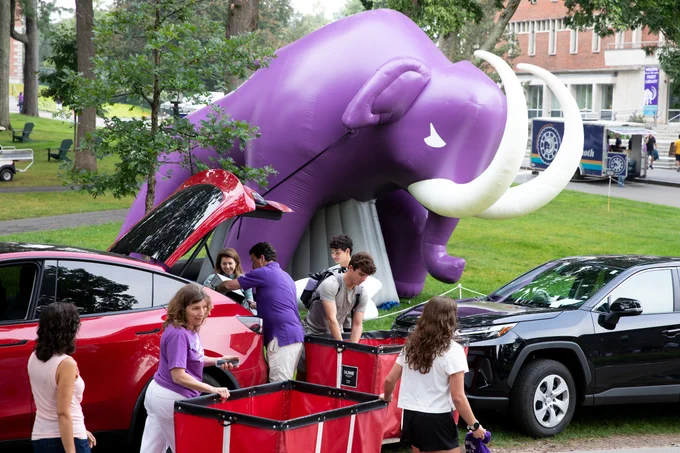 Students and families unpacking cars near the large inflatable purple Mammoth during Move-In Day.