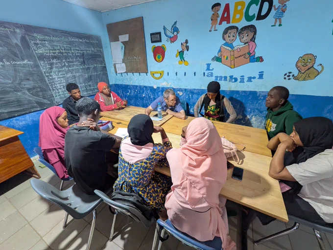 A group of 10 adults sit around a rectangular table, in discussion, in a room with blue walls.