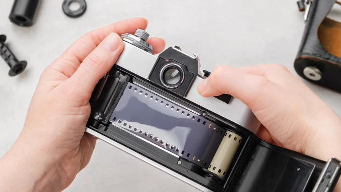 Hands loading film into a retro SLR camera.