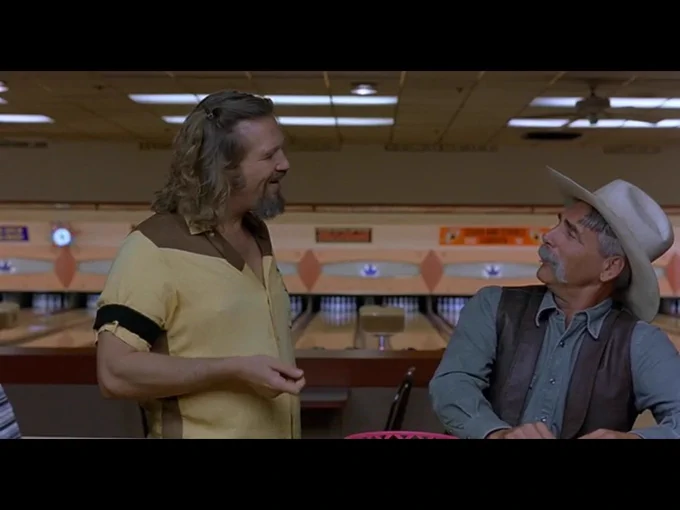 The Dude and the Stranger smile at each other warmly as they converse at the bowling alley bar.