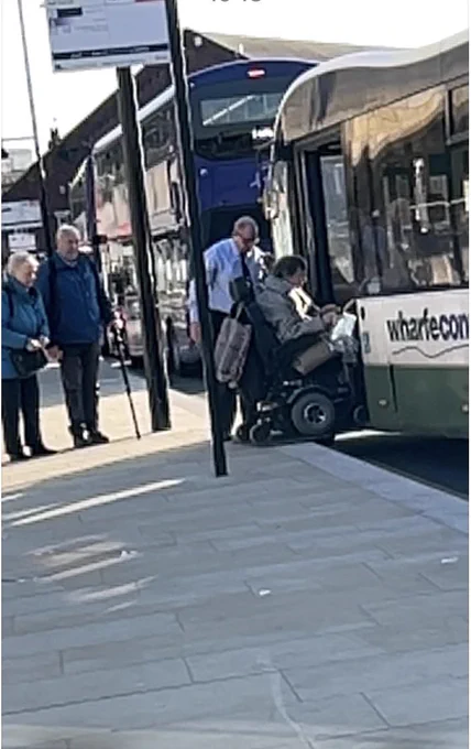 Wheelchair user boarding a connexions bus via the ramp with the driver standing to the side.