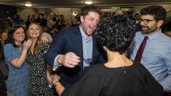 A group of people in business attire celebrating joyfully in a crowded event hall.
