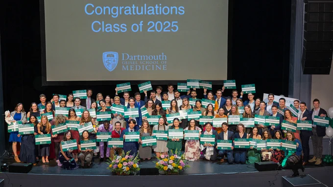 The Dartmouth Geisel School of Medicine Class of 2025 hold certificates on stage, with "Congratulations Class of 2025" displayed on a screen behind them.