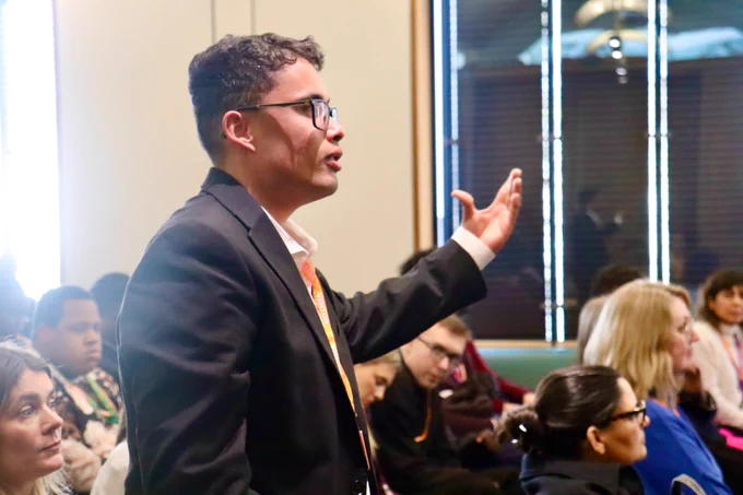 This is an image of a young person standing up, with his arm extended, mid speech