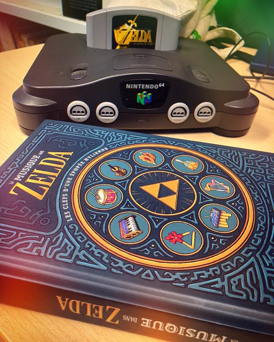 La réédition de mon livre La musique dans Zelda – Les clefs d’une épopée hylienne (édité par Third Éditions) au premier plan. Au second plan, une Nintendo 64 noire avec Zelda Ocarina of Time dedans