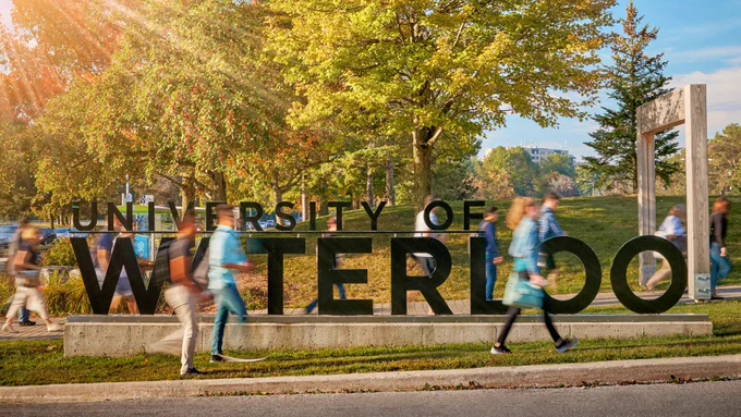 The University of Waterloo sign with students walking by