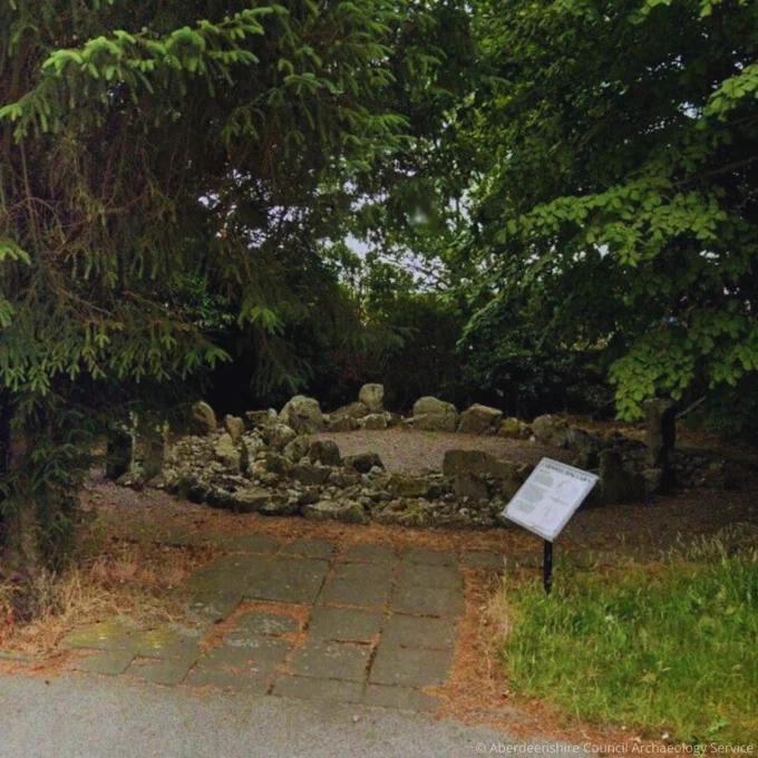 Photo of a bronze age ring cairn on a modern housing estate with an interpretation board nearby
